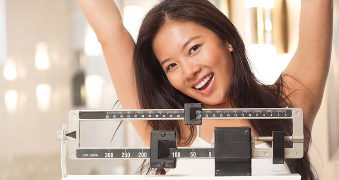 woman on scale with arms in the arm smiling and happy after losing weight